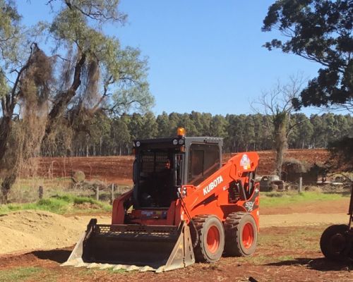 A Red Kubota Skid Steer is Parked in a Dirt Field — Dino's Bobcat–Bitumen & Excavator Hire in Cushnie, QLD