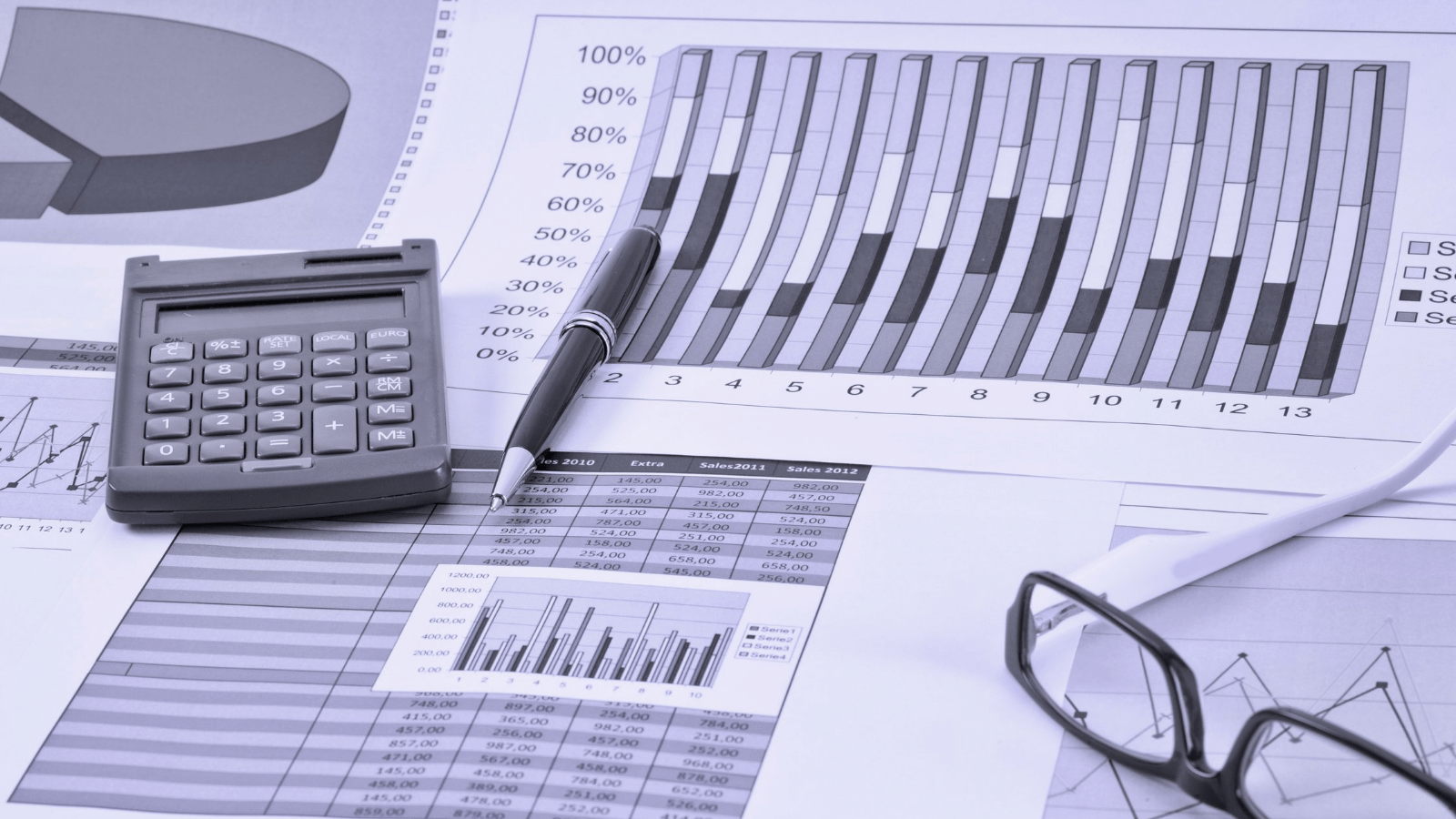 Calculator and eyeglasses on financial charts with a pen and pie chart in the background