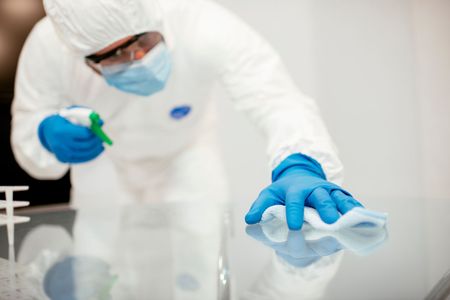 Person mopping a tiled hallway floor with a blue mop and bucket nearby
