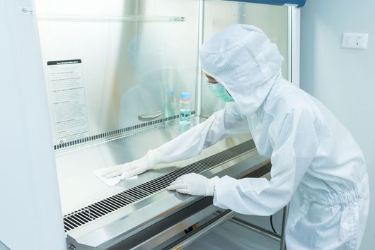 Lab worker in white protective suit operating a biosafety cabinet in a clean laboratory.