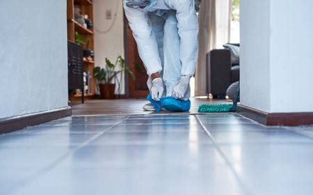 Person mopping a tiled hallway floor with a blue mop and bucket nearby