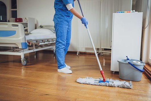 Hospital worker mopping a wooden floor beside a bed and cleaning bucket