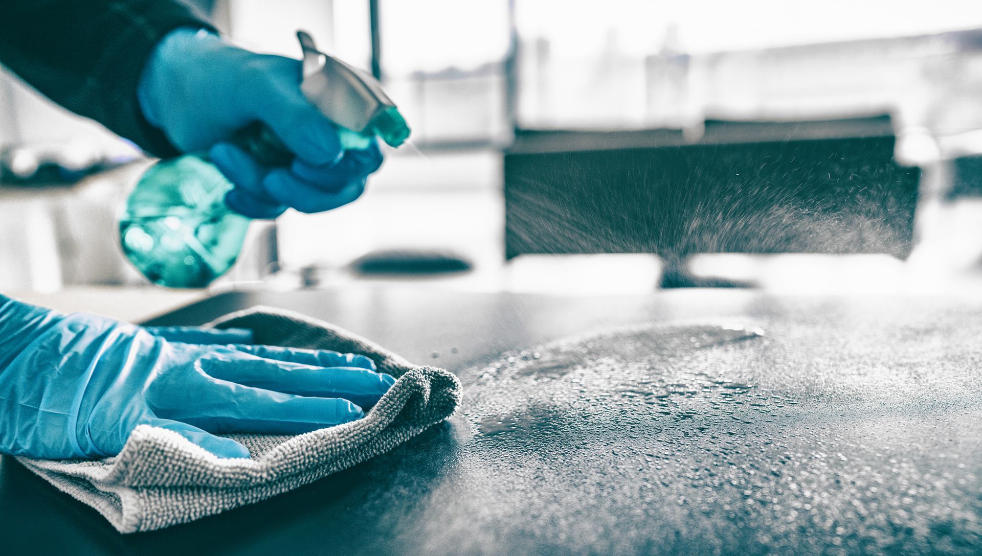 Gloved hands spray disinfectant and wipe a countertop with a cloth