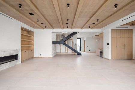 Modern open-plan living room with wood ceiling, staircase, and large windows