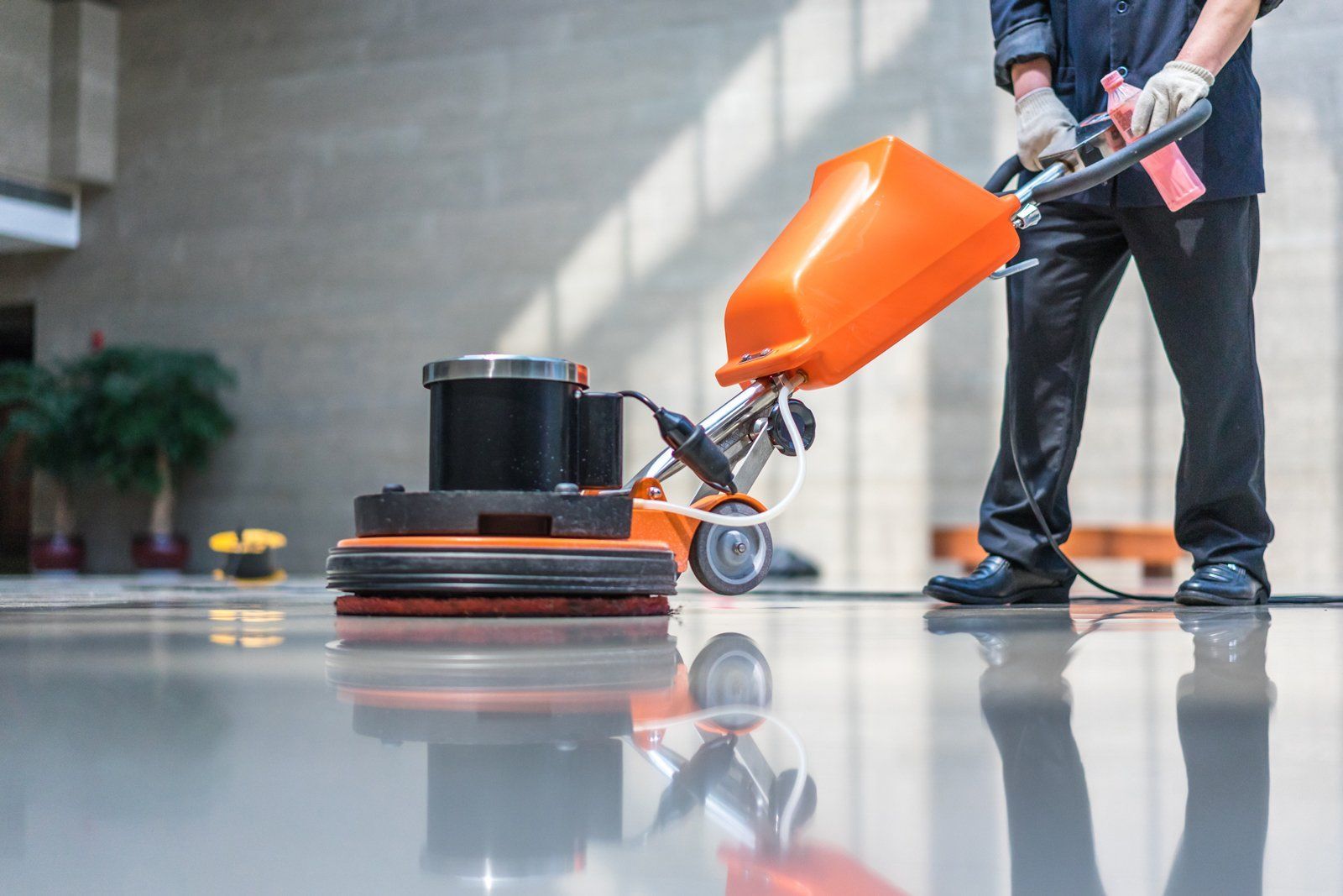 Person using an orange floor scrubber on a glossy indoor floor