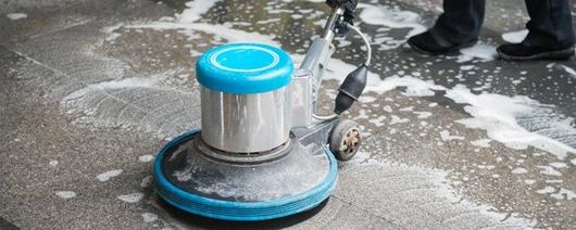 Floor scrubber cleaning a wet concrete surface with white foam around it
