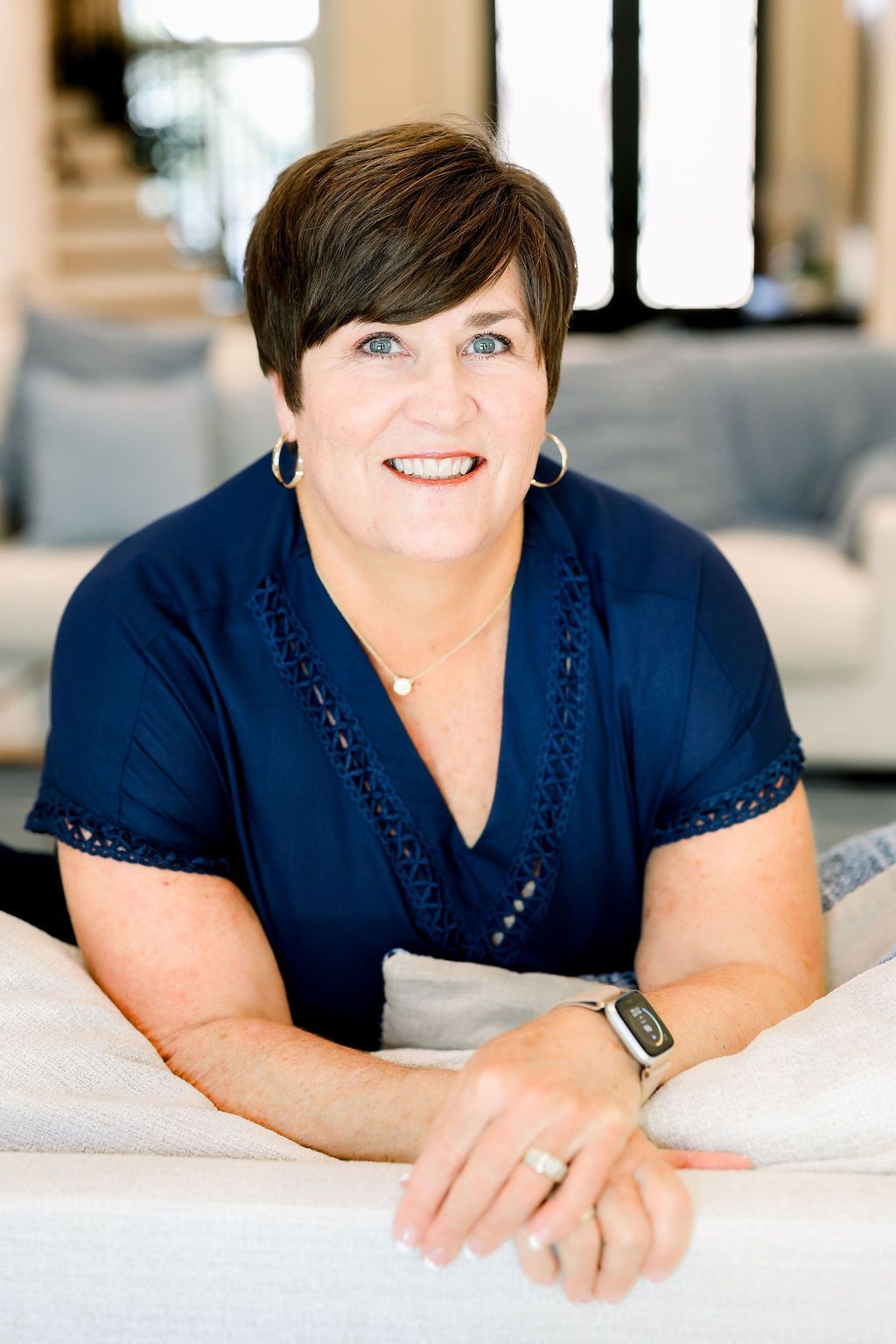 Woman with short brown hair smiles, wearing black shirt, against a dark background.