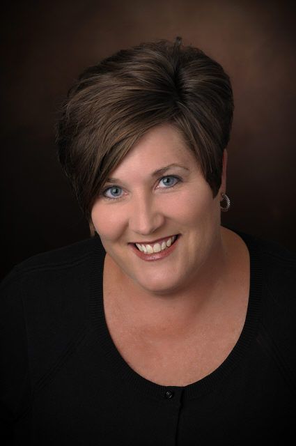 A woman with short brown hair and blue eyes is smiling for the camera.