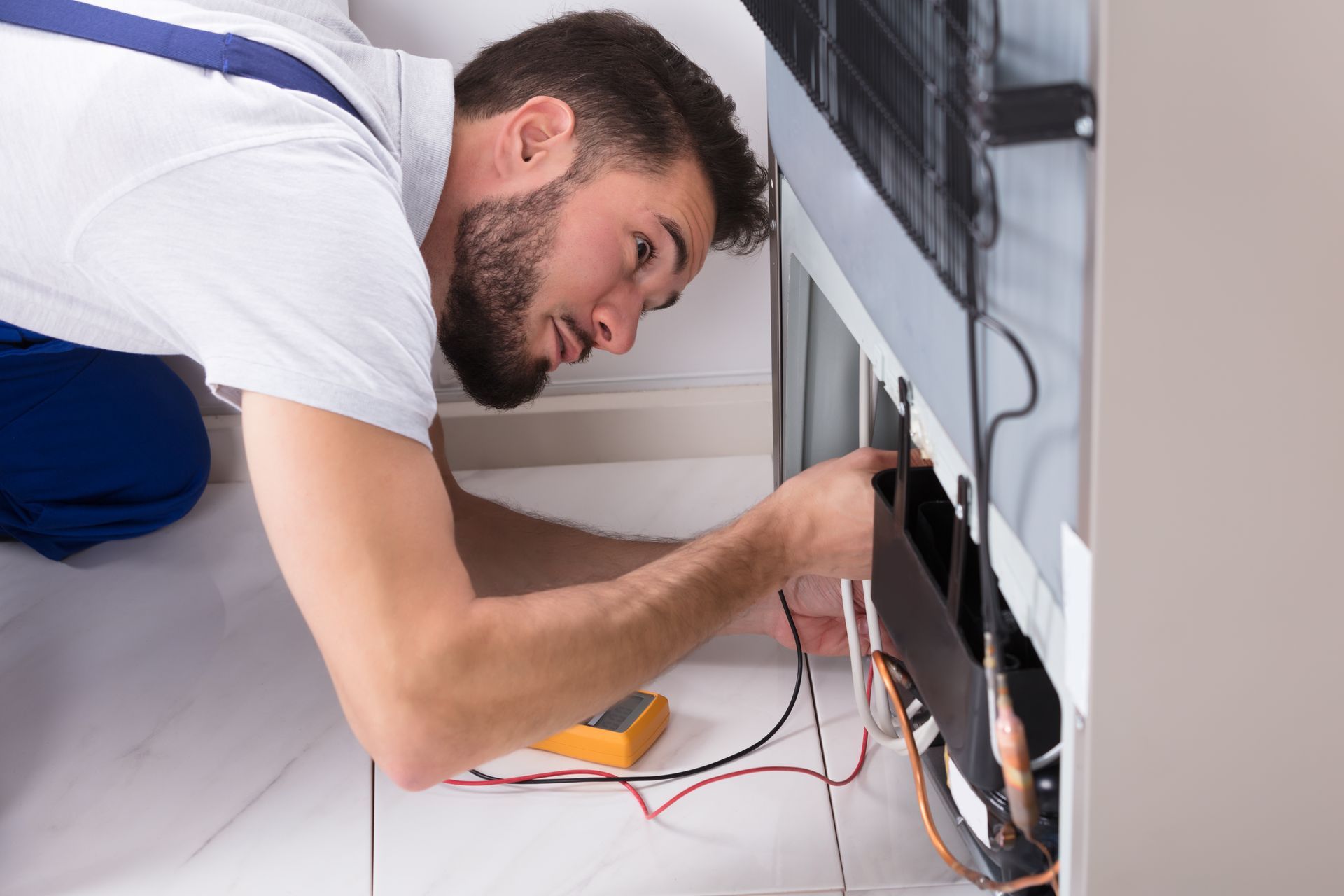 Technician using digital multimeter to inspect refrigerator components.
