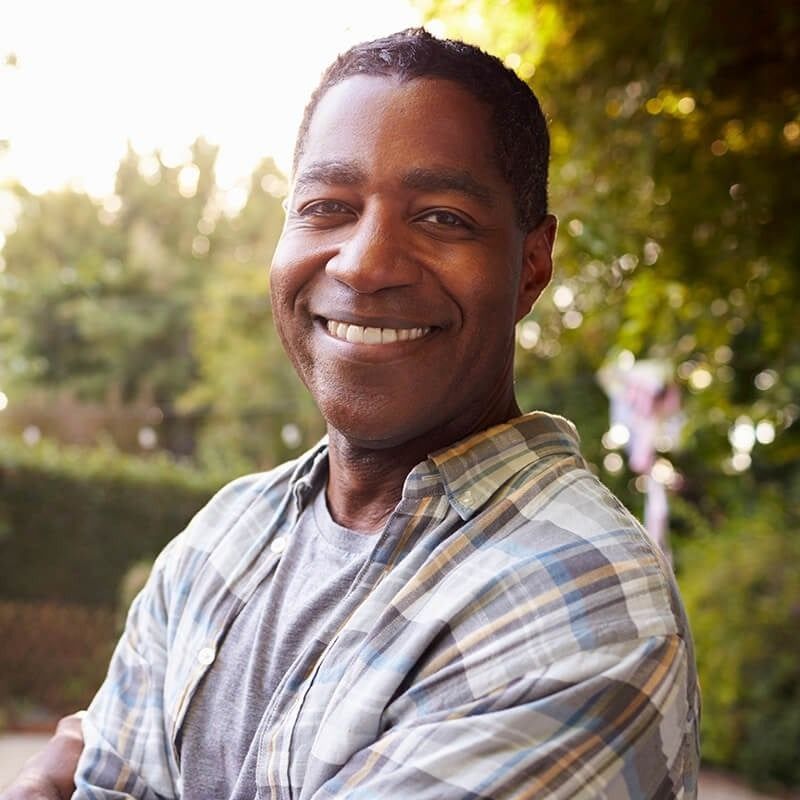 A man in a plaid shirt is smiling with his arms crossed.