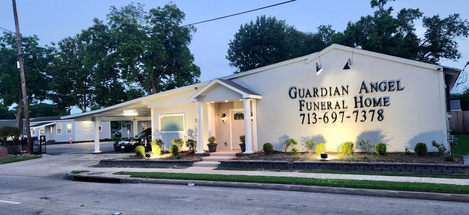 Guardian Angel Funeral Home, light-colored building with sign, phone number, and street view. Evening, trees in background.