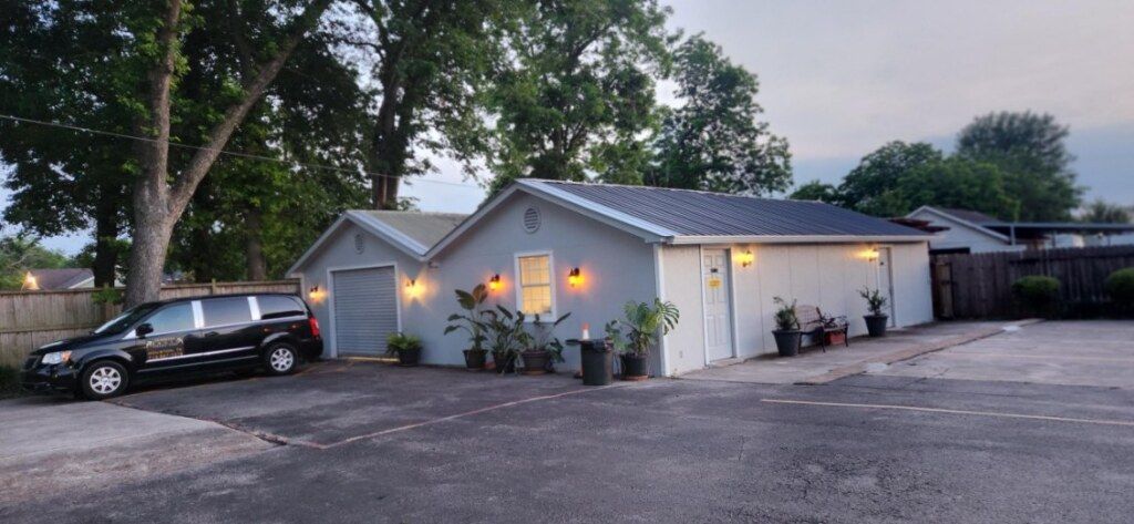 Exterior view of a building with a black vehicle parked in front. Gray building with lighting and potted plants.