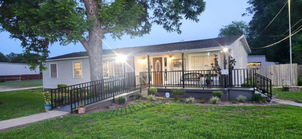 A small house with a porch, a tree and a walkway, at dusk. Green grass and blue sky.