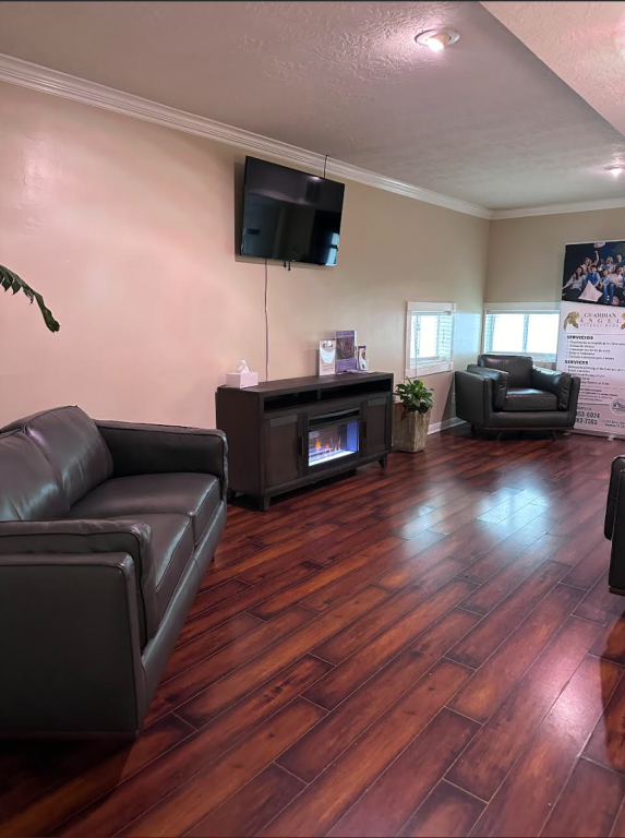 Waiting room with a dark leather sofa, armchair, fireplace, TV, and wood flooring.