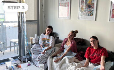 Three women are sitting on a bed in a living room.