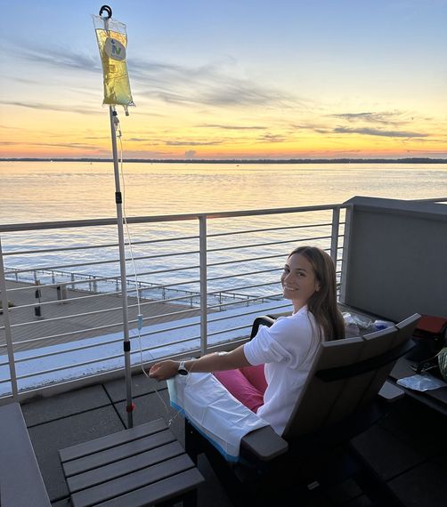 A woman is sitting on a chair on a balcony overlooking the ocean.