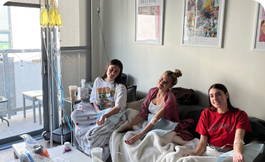 Three women are sitting on a bed with iv drips in a living room.