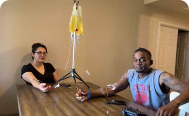 A man and a woman are sitting at a table with iv drips in their hands.