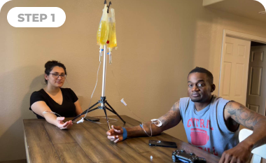 A man and a woman are sitting at a table with an iv in their arm.