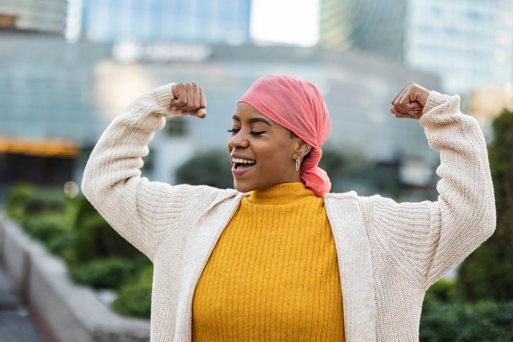 A woman wearing a pink head scarf is flexing her muscles.