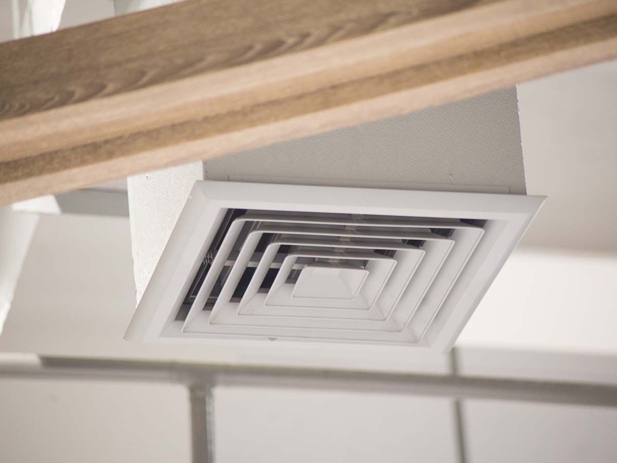 A close up of a square air vent on the ceiling of a room.