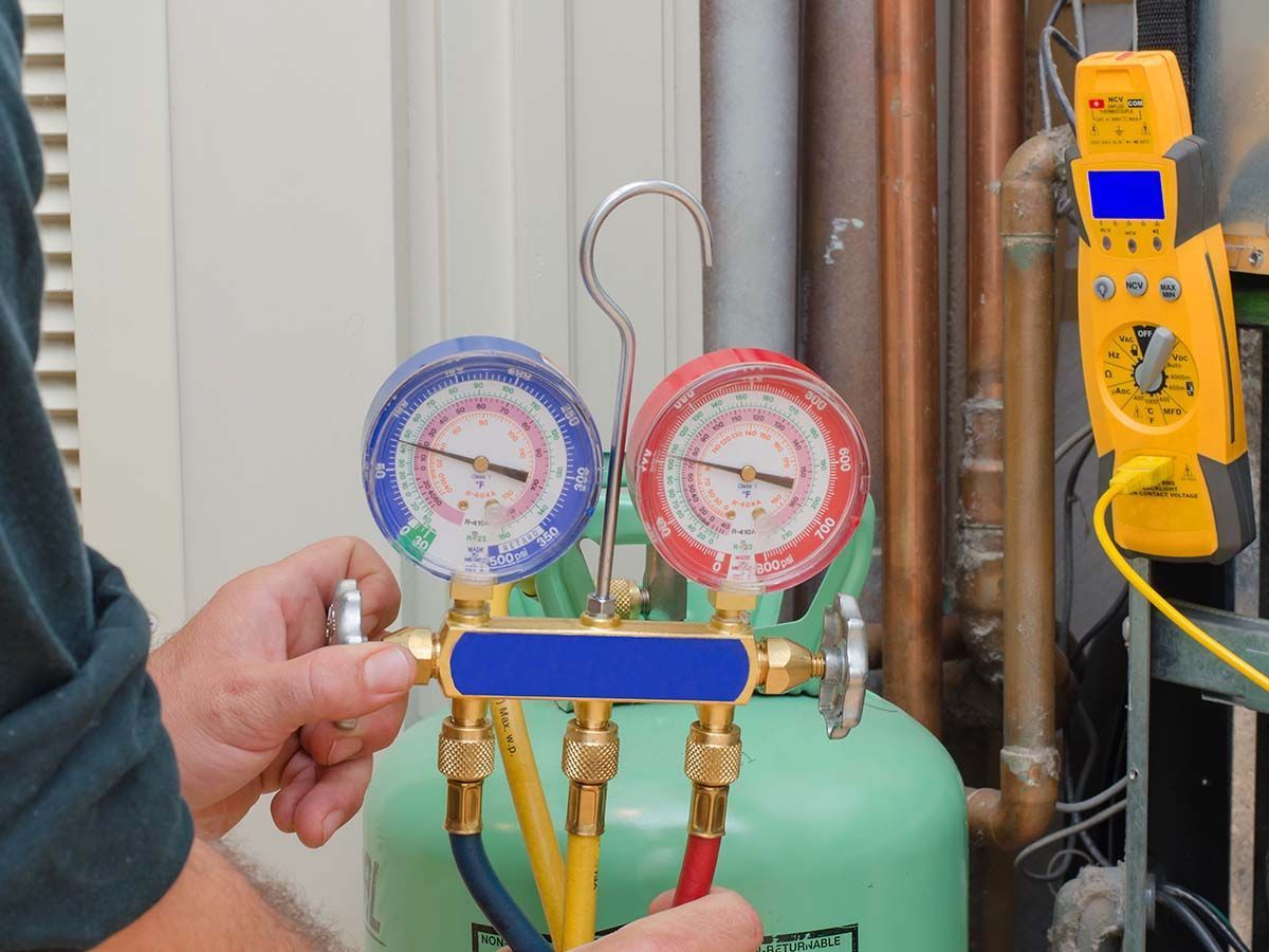 A man is holding a gauge while working on an air conditioner.