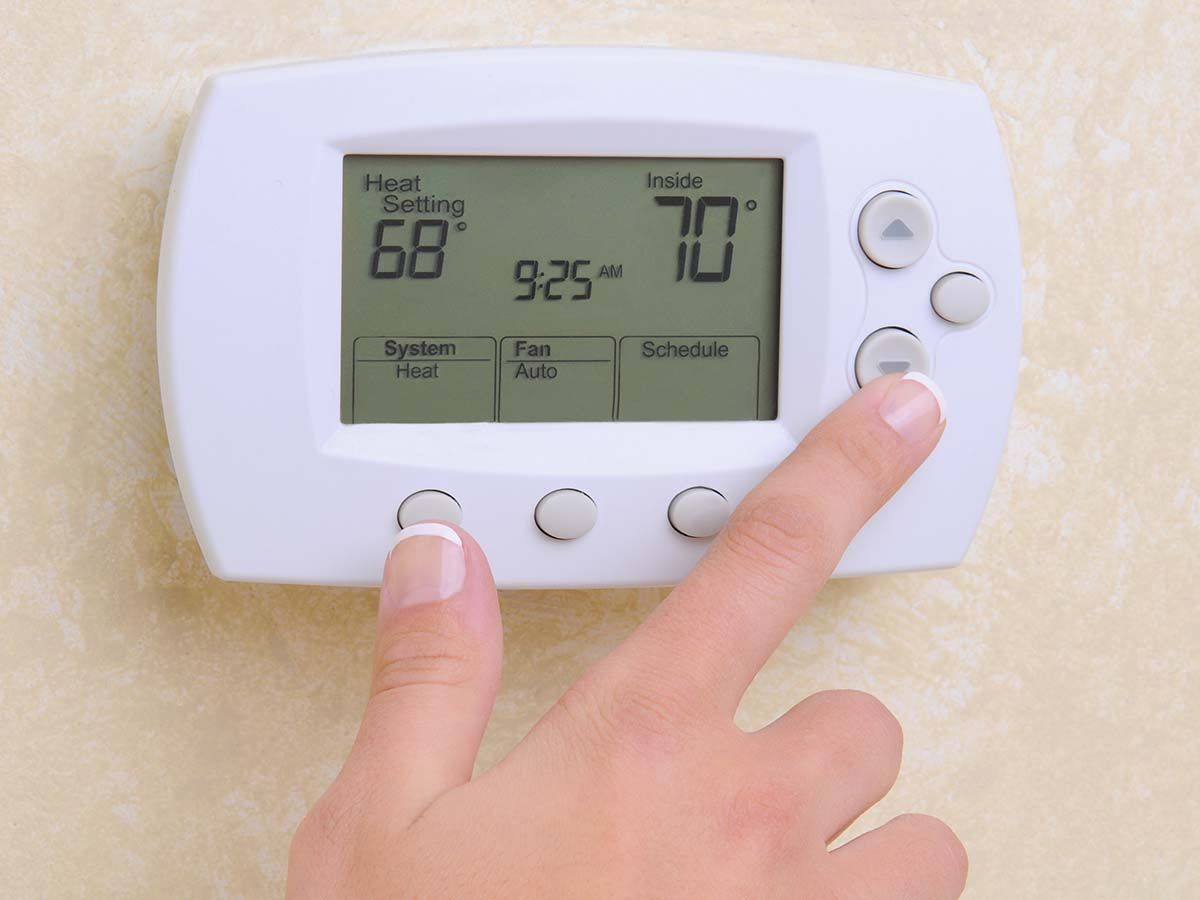 A person is pressing a button on a thermostat that is set to 70 degrees