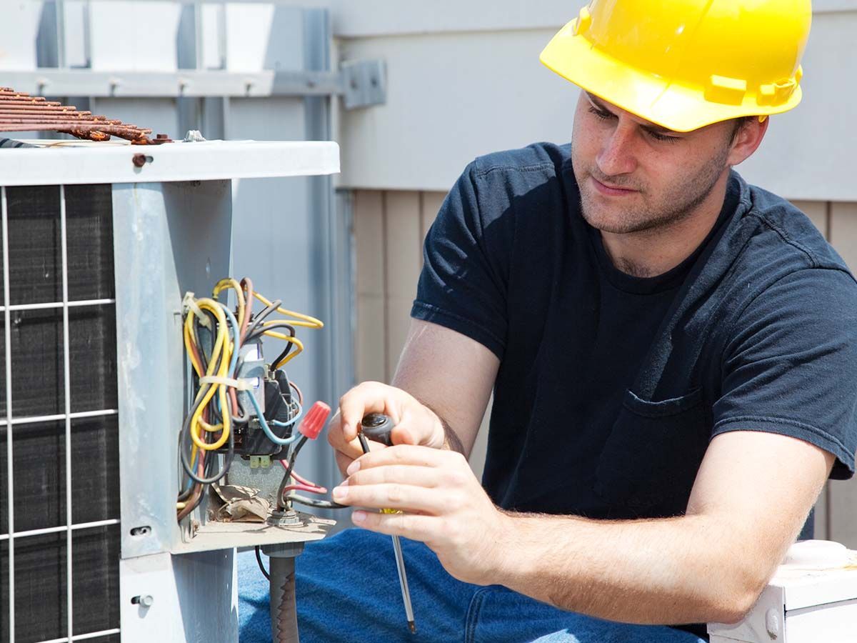 A man wearing a hard hat is working on an air conditioner.