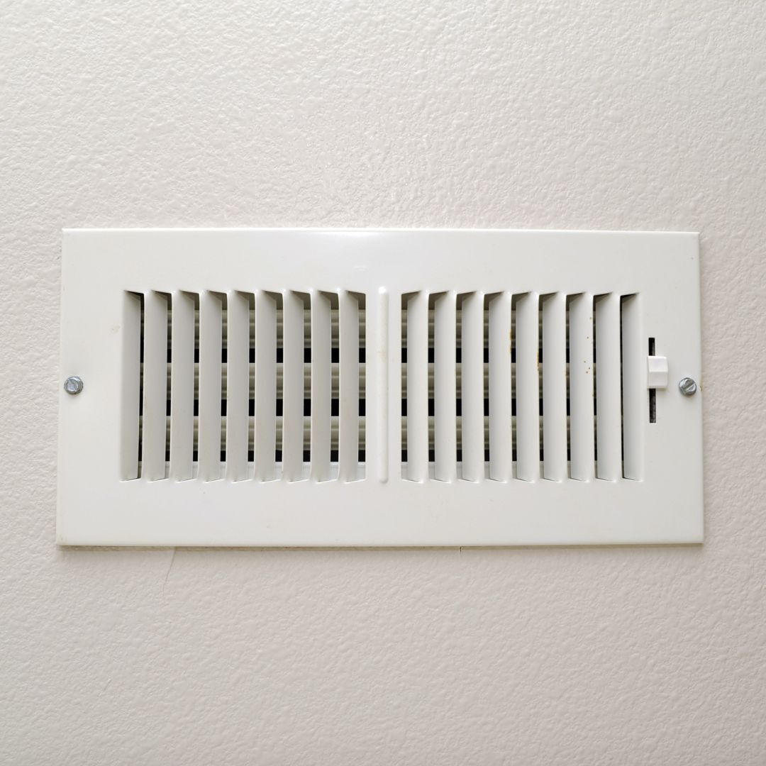 A white air vent is hanging on a white wall.