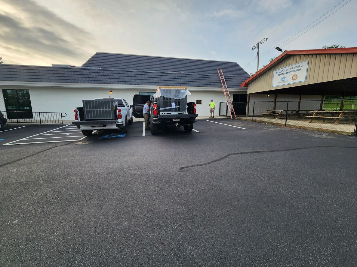 Two trucks parked in front of a building, possibly a business, with workers and a ladder visible.