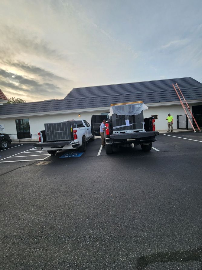 Trucks parked in front of a building. Workers are unloading items. Asphalt parking lot and cloudy sky.