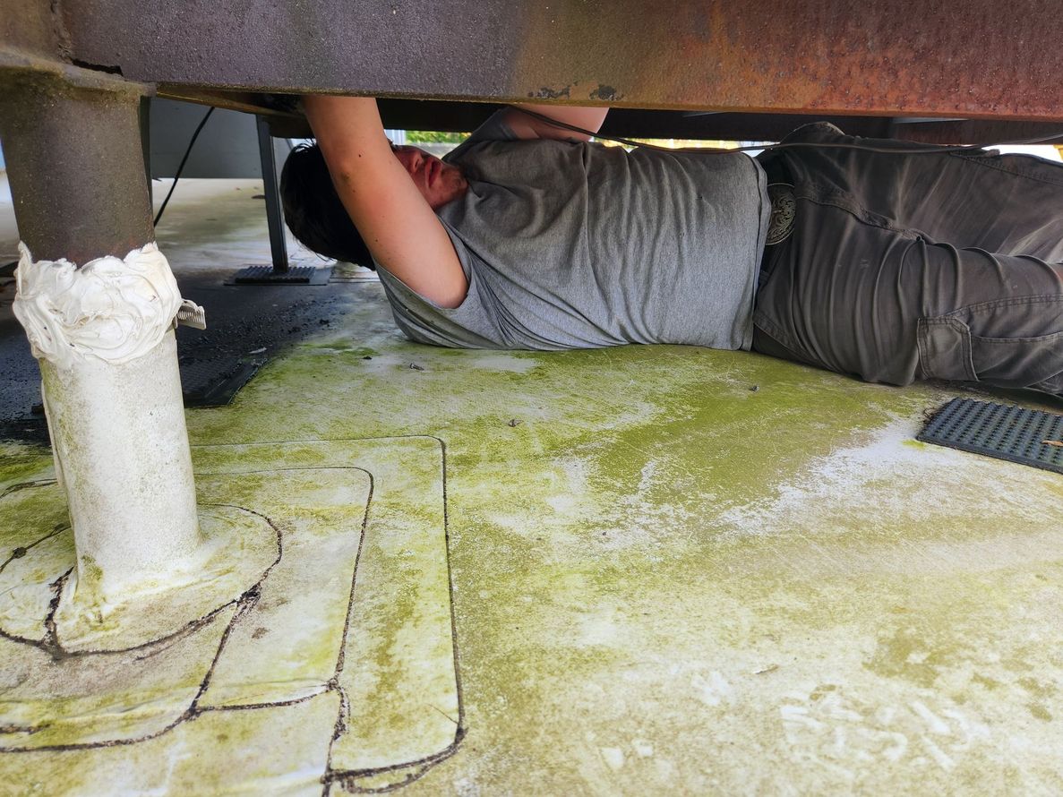 Person lying under structure, reaching up. Ground is stained green.