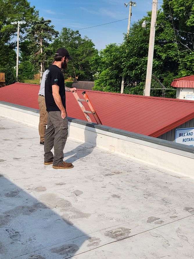 Two men standing on a flat, white roof, looking at a red curved roof. Daylight setting.