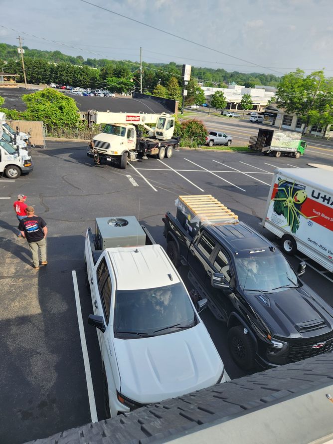 Parking lot with trucks, including a white pickup, a moving truck, and a flatbed. People are present.