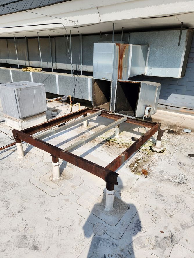 Metal frame on a rooftop, possibly for HVAC equipment. Ductwork and a shadow are also visible.