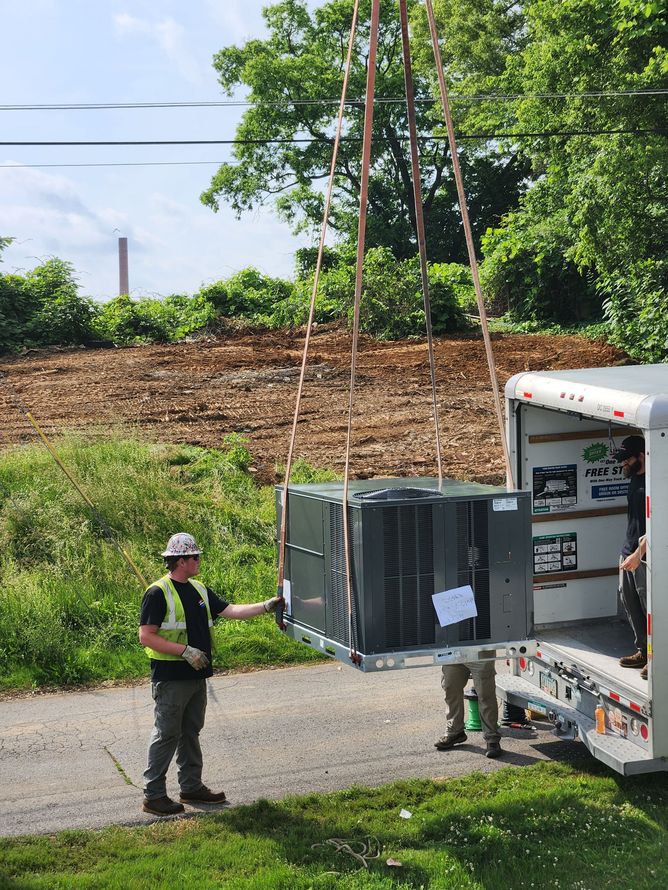 Workers lift an air conditioning unit into a truck with a pulley system, outdoors.