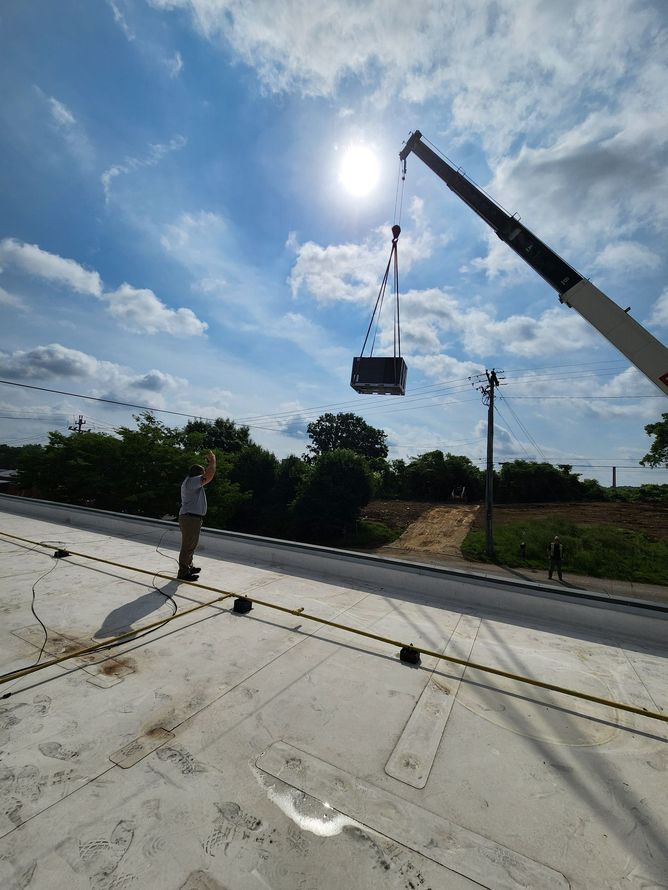A crane lifting a rectangular object on a rooftop under a bright sun. A person stands nearby.