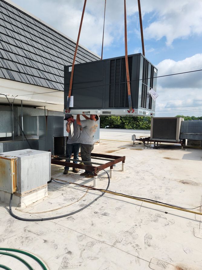HVAC unit being lifted onto a roof by a crane. A worker stands nearby.