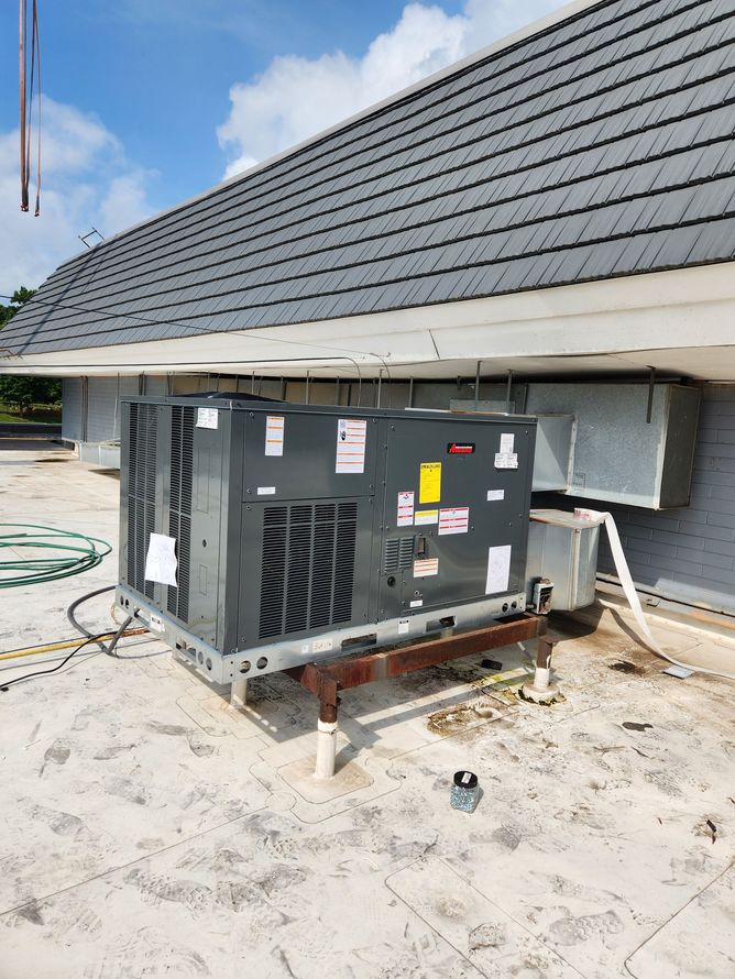 A rooftop HVAC unit on a flat roof. Gray unit, white roof, gray shingles, blue sky.