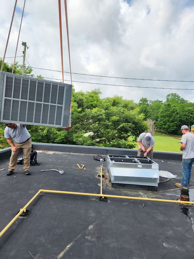 Workers installing HVAC unit on a rooftop under cloudy sky. One man holds a grate while others work on the base.