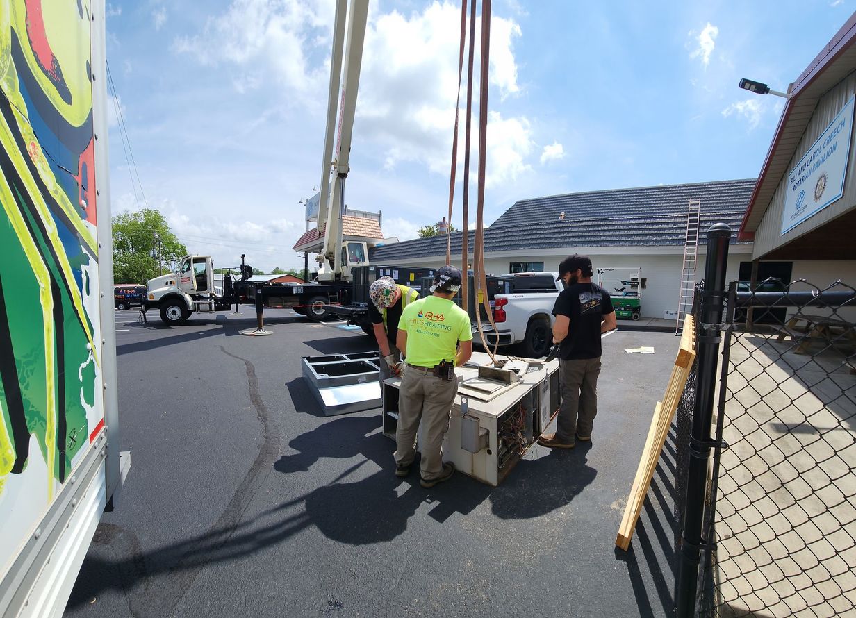 Construction workers installing equipment near a building with a crane, truck, and sunny sky.
