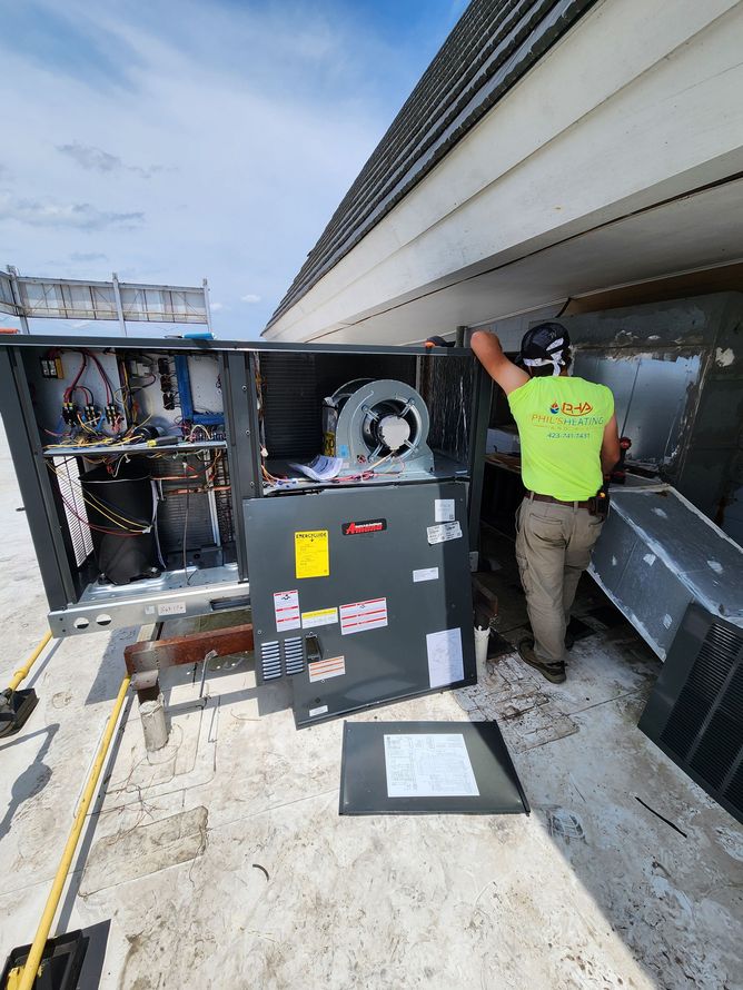 HVAC technician in a safety vest working on rooftop air conditioning unit. Blue sky.