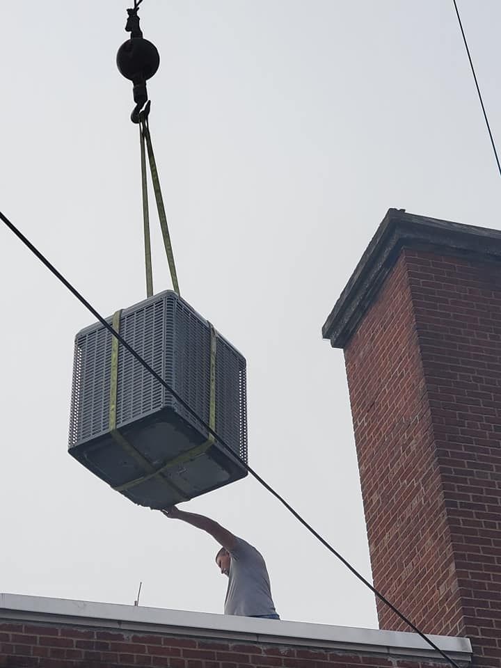A man is standing on a roof holding a box that is being lifted by a crane