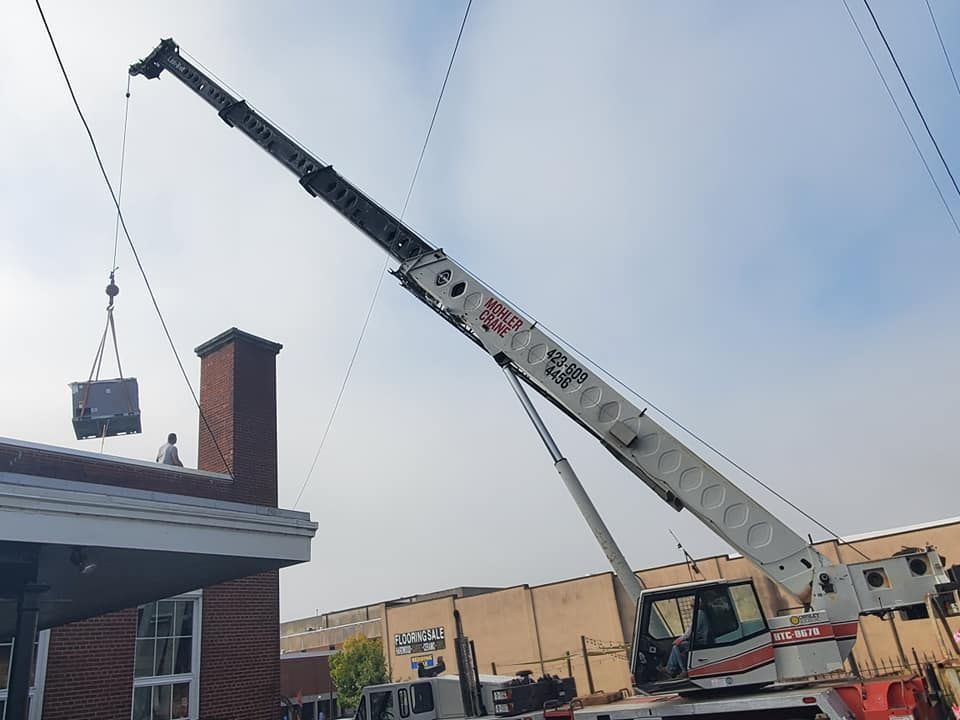 A large crane is lifting a box from the roof of a building.