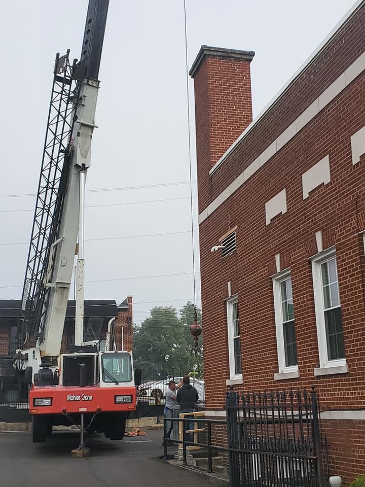 A crane is lifting a chimney in front of a brick building