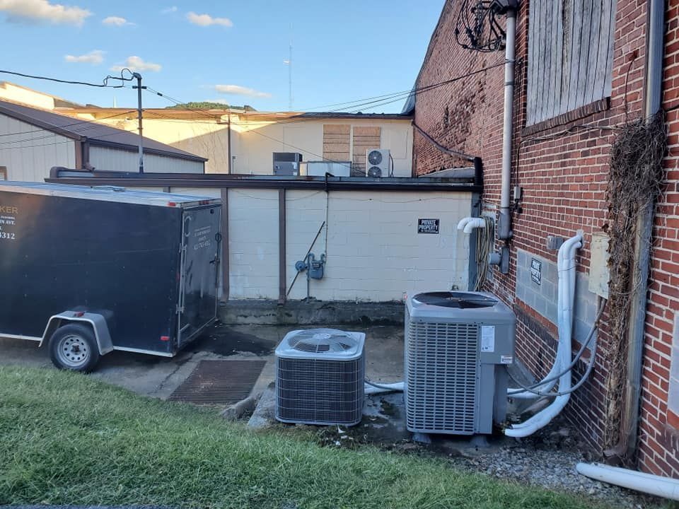 A black trailer is parked in front of a brick building with air conditioners.