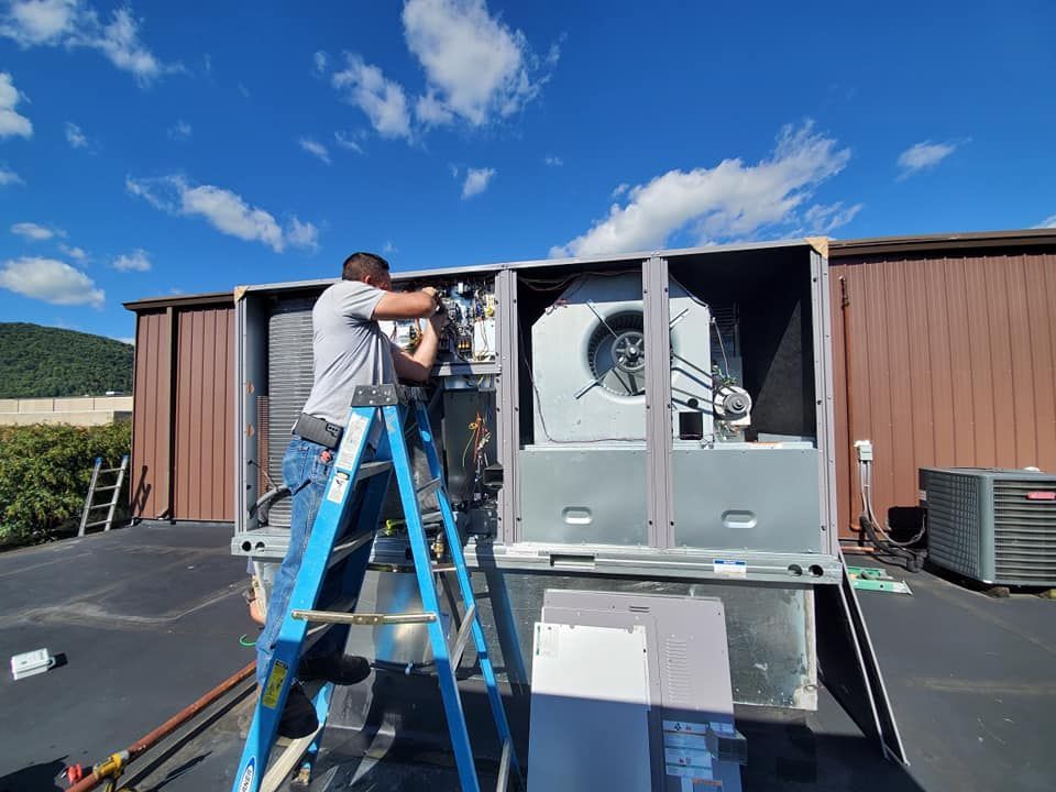 A man is standing on a ladder working on an air conditioner.