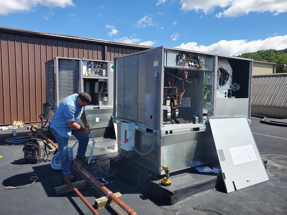 A man is working on an air conditioner on the roof of a building.