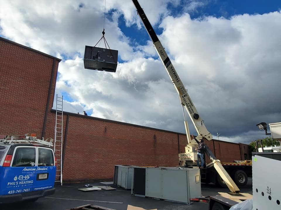 A crane is lifting a box in the air in front of a brick building.