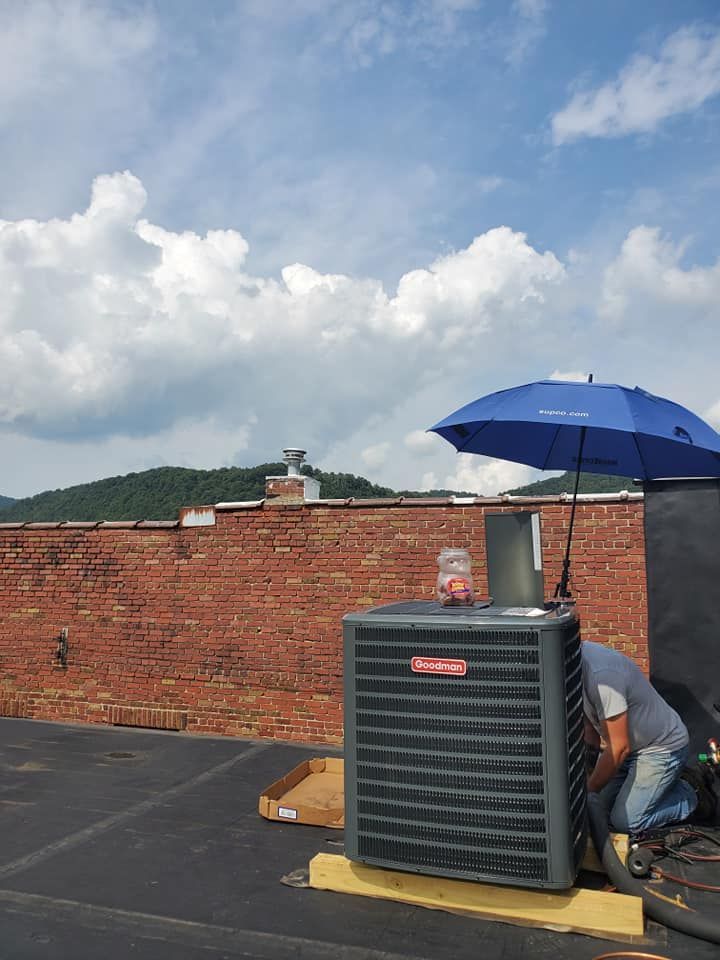 A man is working on an air conditioner on a roof with an umbrella